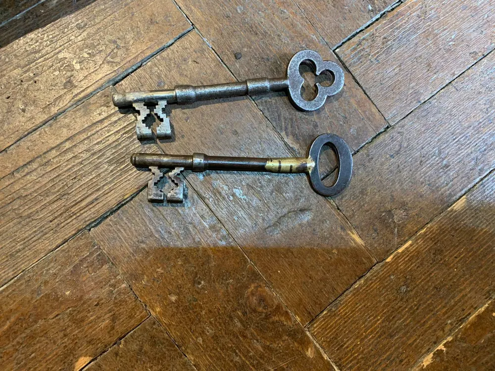 Two antique mortice keys with ornate bows resting on a parquet wood floor