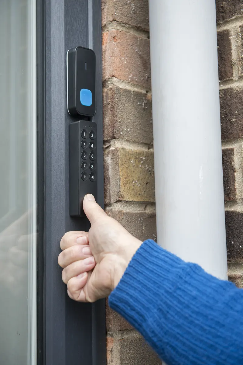 Hand entering a code on a wall mounted key safe keypad beside a grey front door