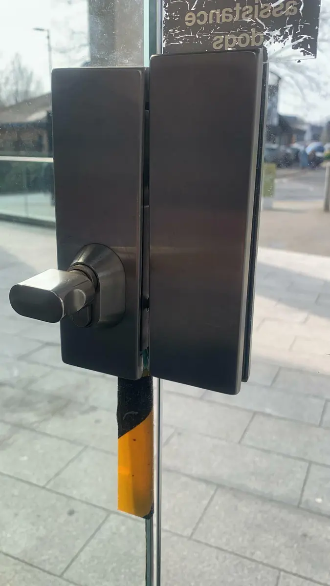 Gunmetal patch lock with oval thumb turn fitted to a frameless glass commercial door