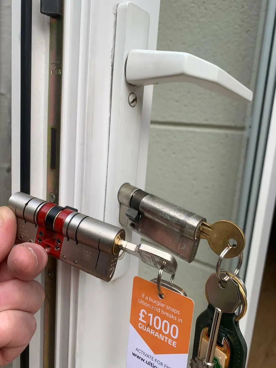 Locksmith holding a new anti-snap euro cylinder beside the worn cylinder on a white uPVC door, Ultion tag