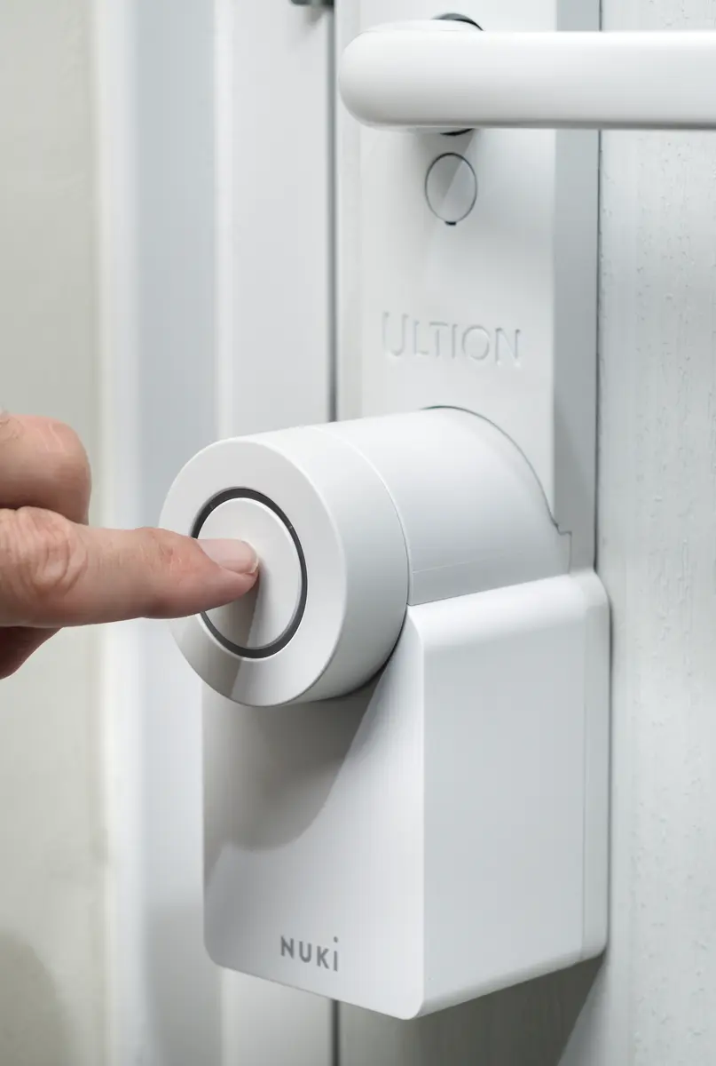 White Ultion Nuki smart lock on a front door with a finger pressing the unlock button