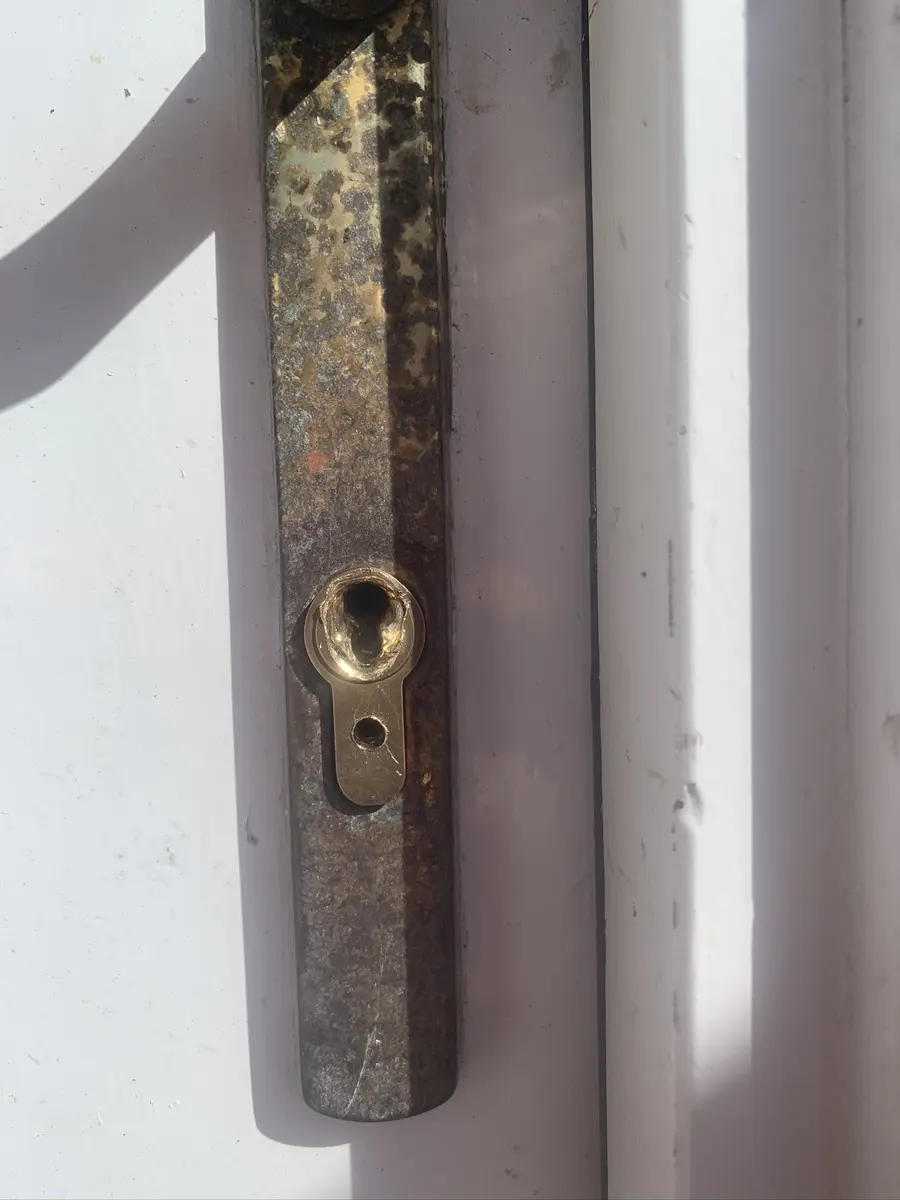 New brass euro cylinder fitted through an older weathered handle backplate on a white timber door