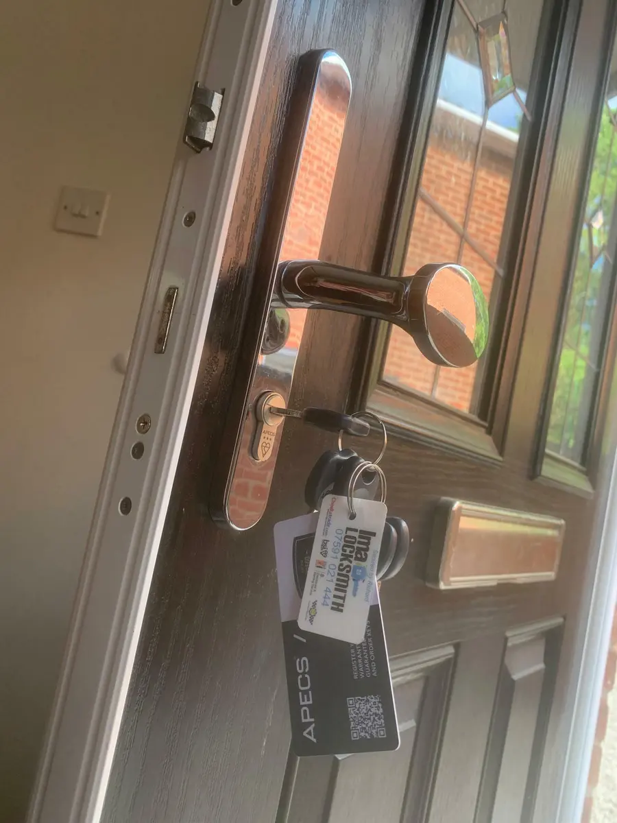 Chrome pad handle and APECS anti-snap cylinder on a dark composite door with keys and Ima Locksmith tag