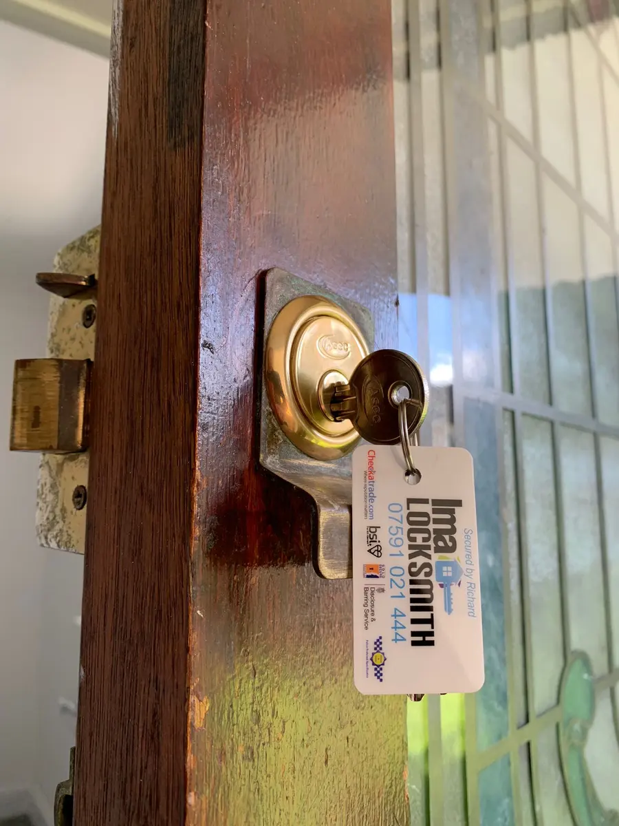 New brass Asec rim cylinder on a dark wooden door with stained glass and Ima Locksmith keyring