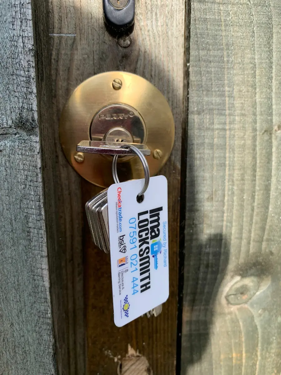 Brass Perry gate lock with key and Ima Locksmith tag on a timber garden gate