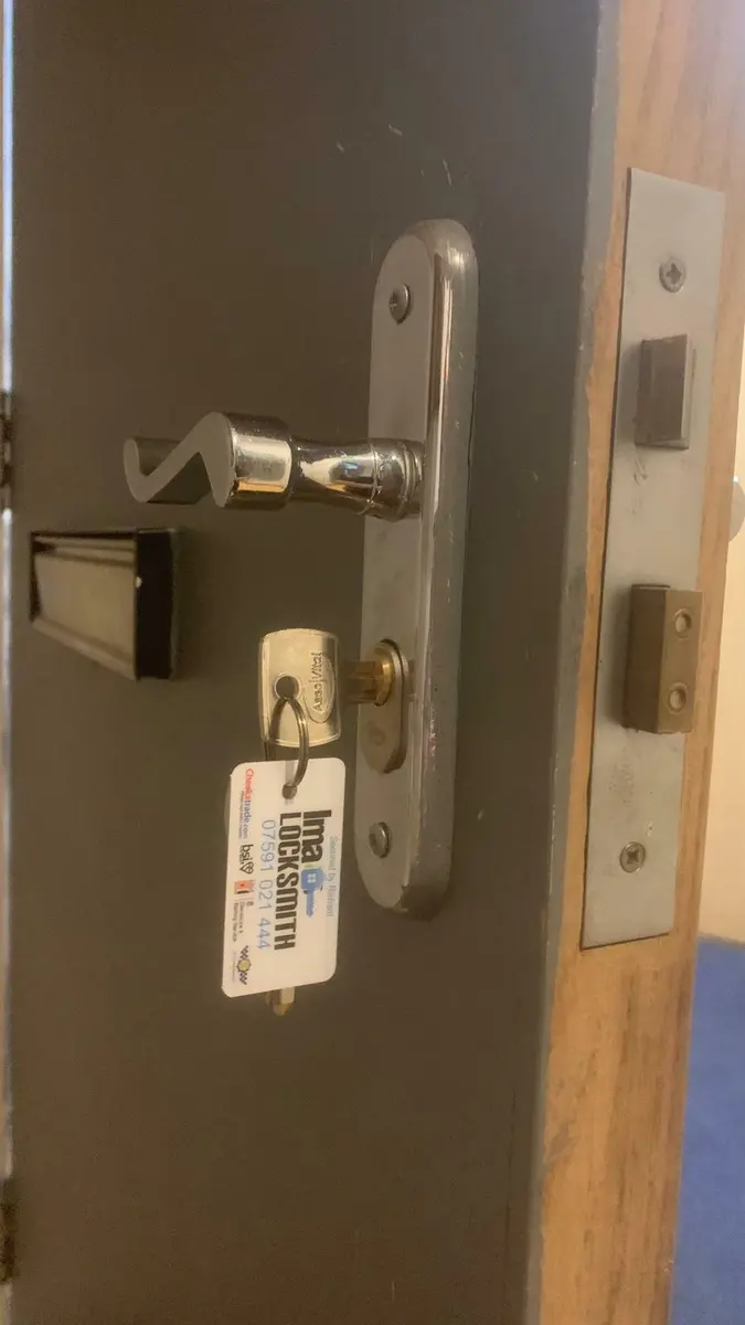 Chrome lever handle and oval cylinder with Ima Locksmith tag on a grey internal door